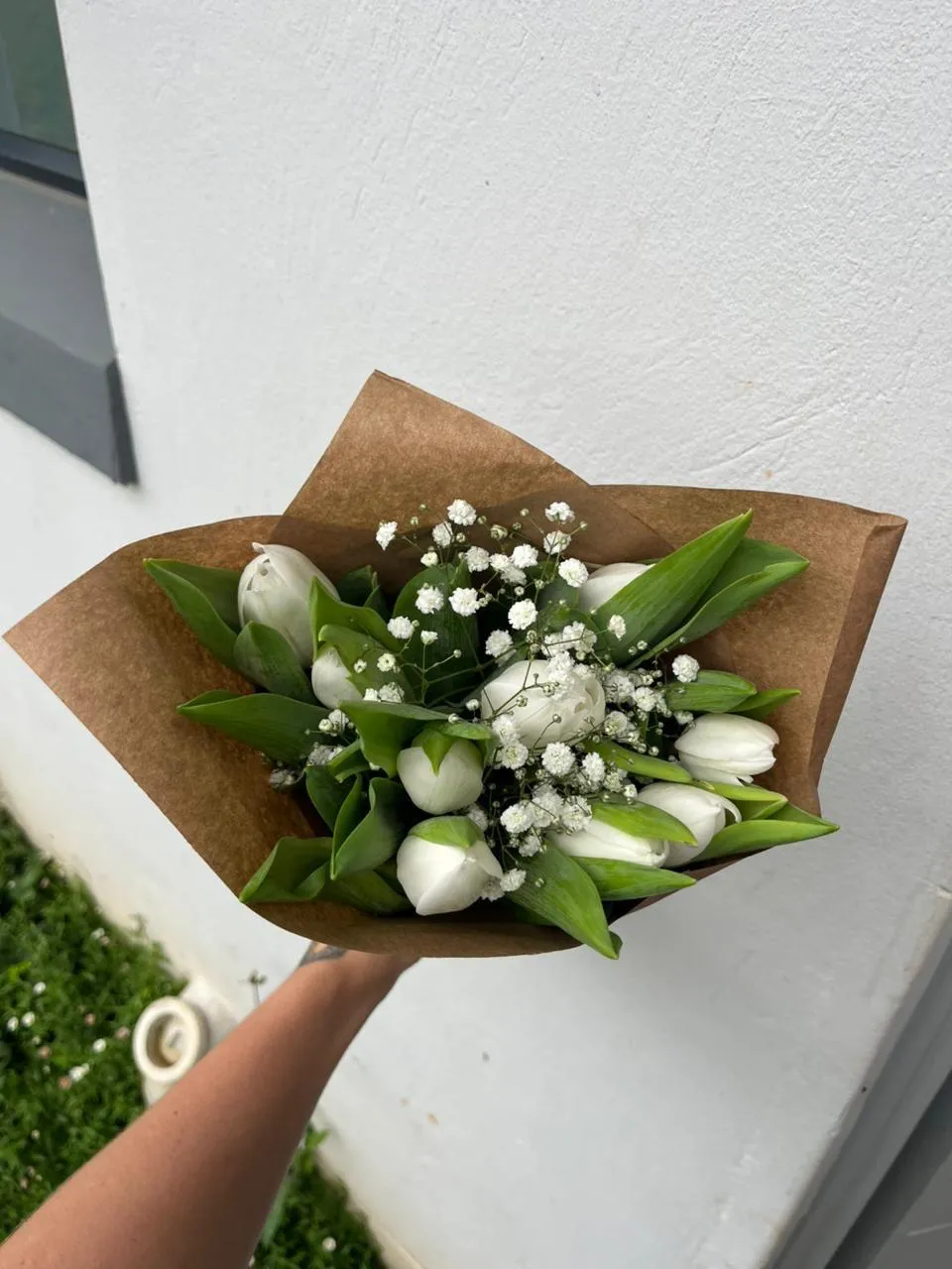 A bouquet of white tulips and baby's breath wrapped in kraft paper