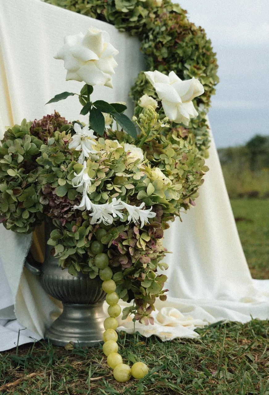 A hydrangea and white rose arrangement in a silver urn, styled outdoors