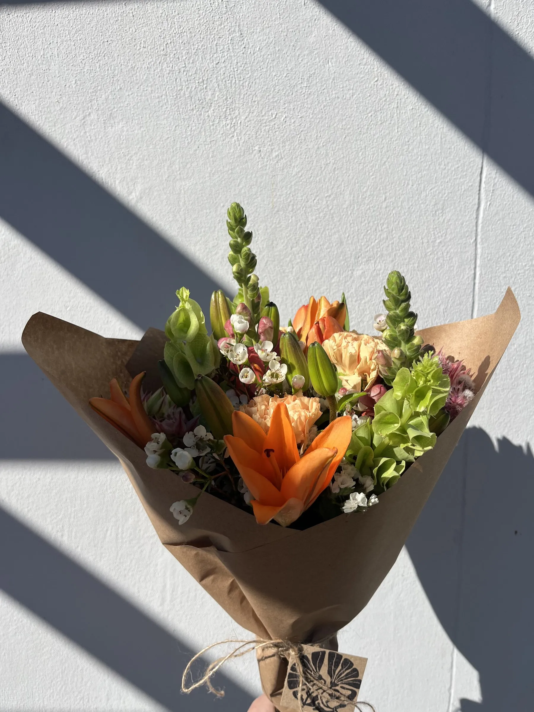 An orange lily and carnation bouquet against a white wall in hard sunlight