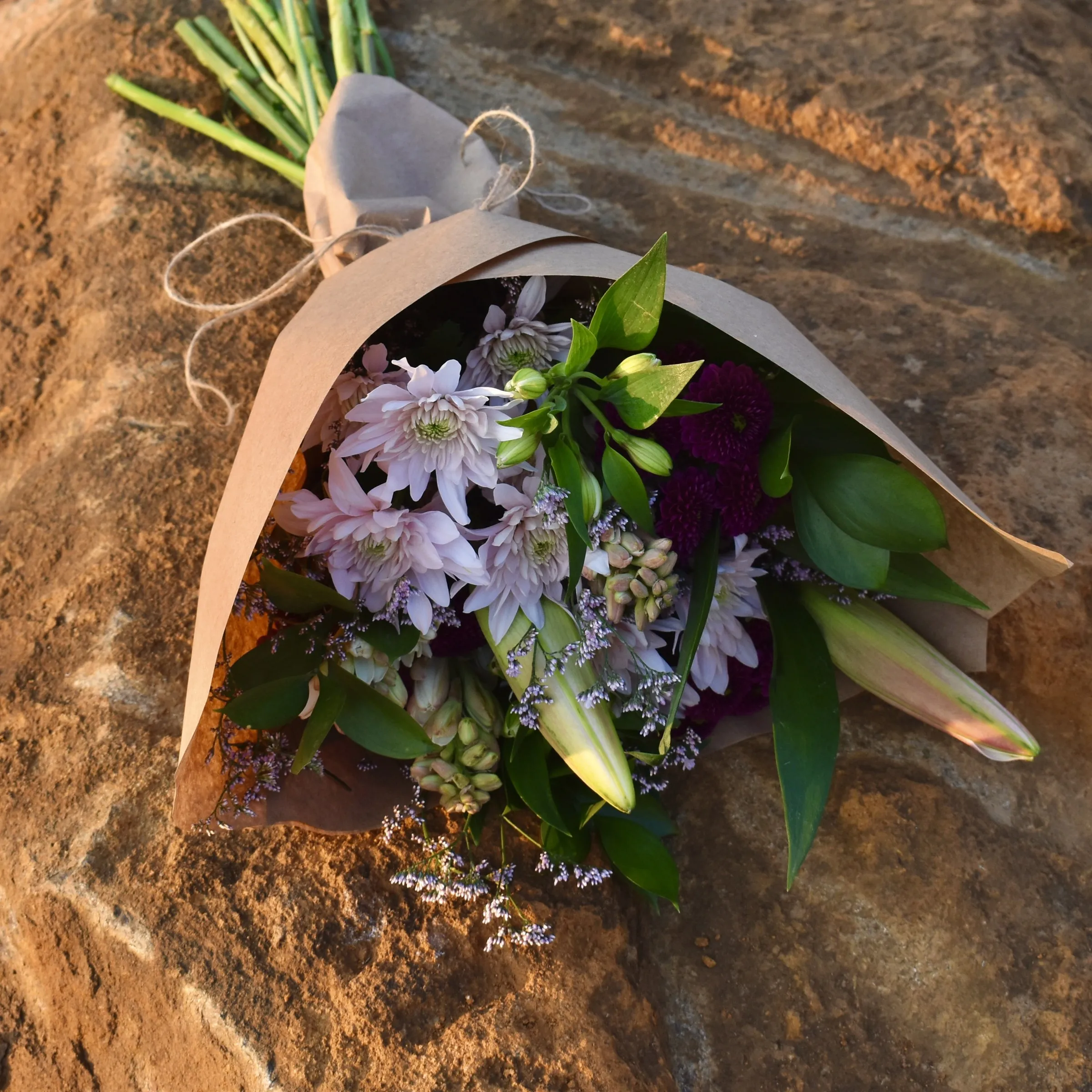 A lilac and burgundy bouquet tied with twine, resting on warm sandstone