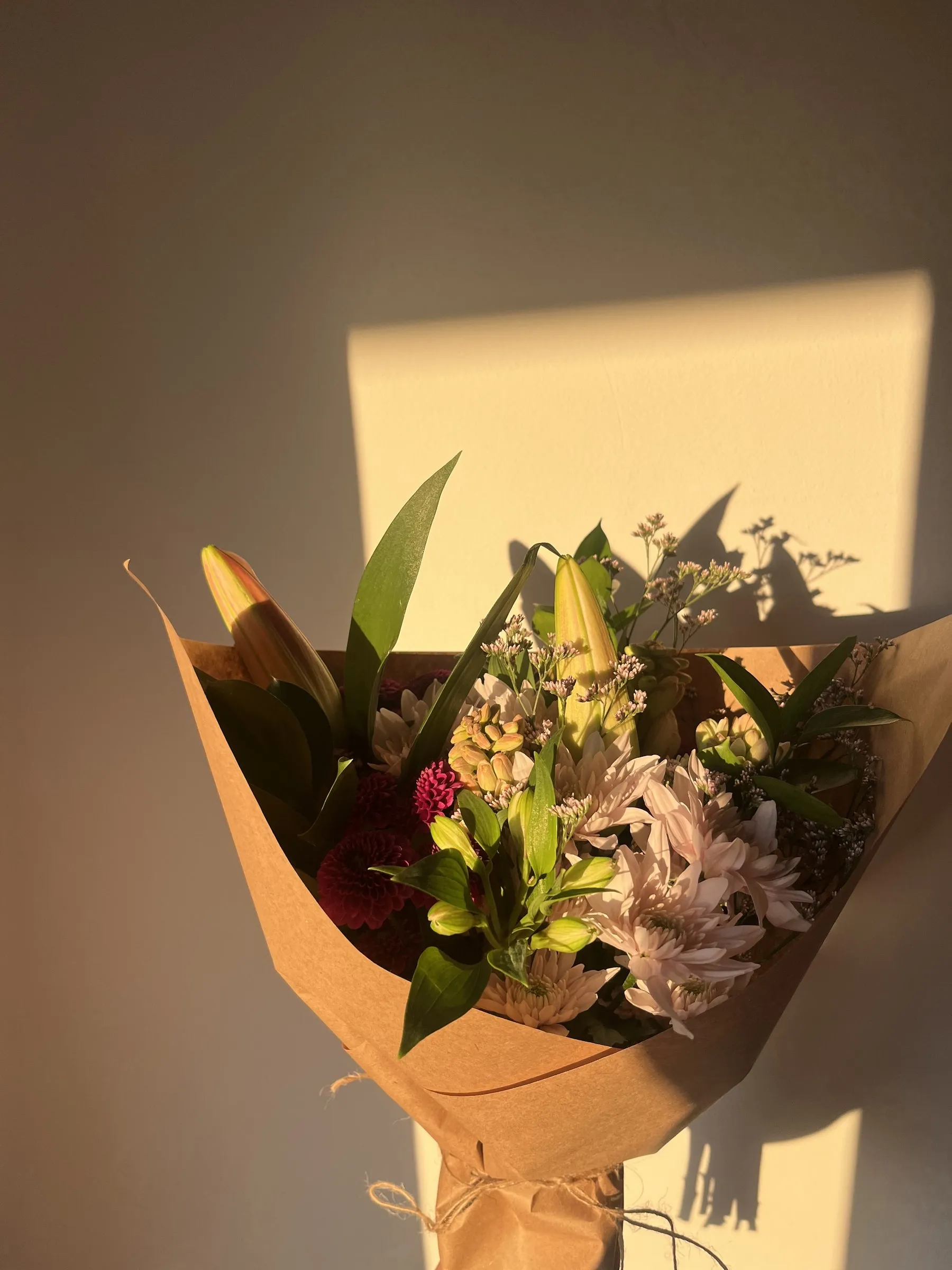 A bouquet of chrysanthemums and lilies in kraft paper, lit by late afternoon sun