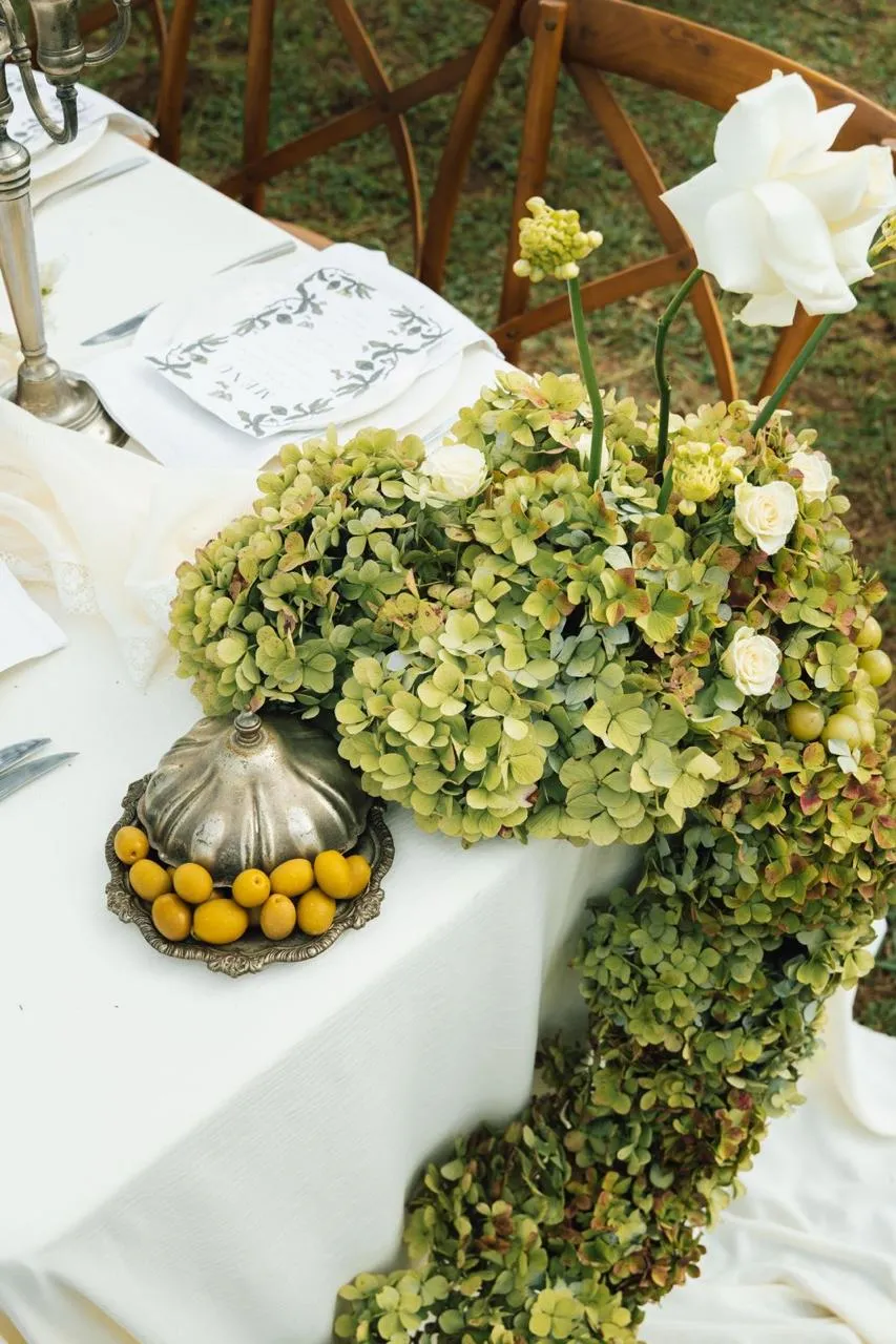 A green hydrangea table runner with white roses on a styled wedding table